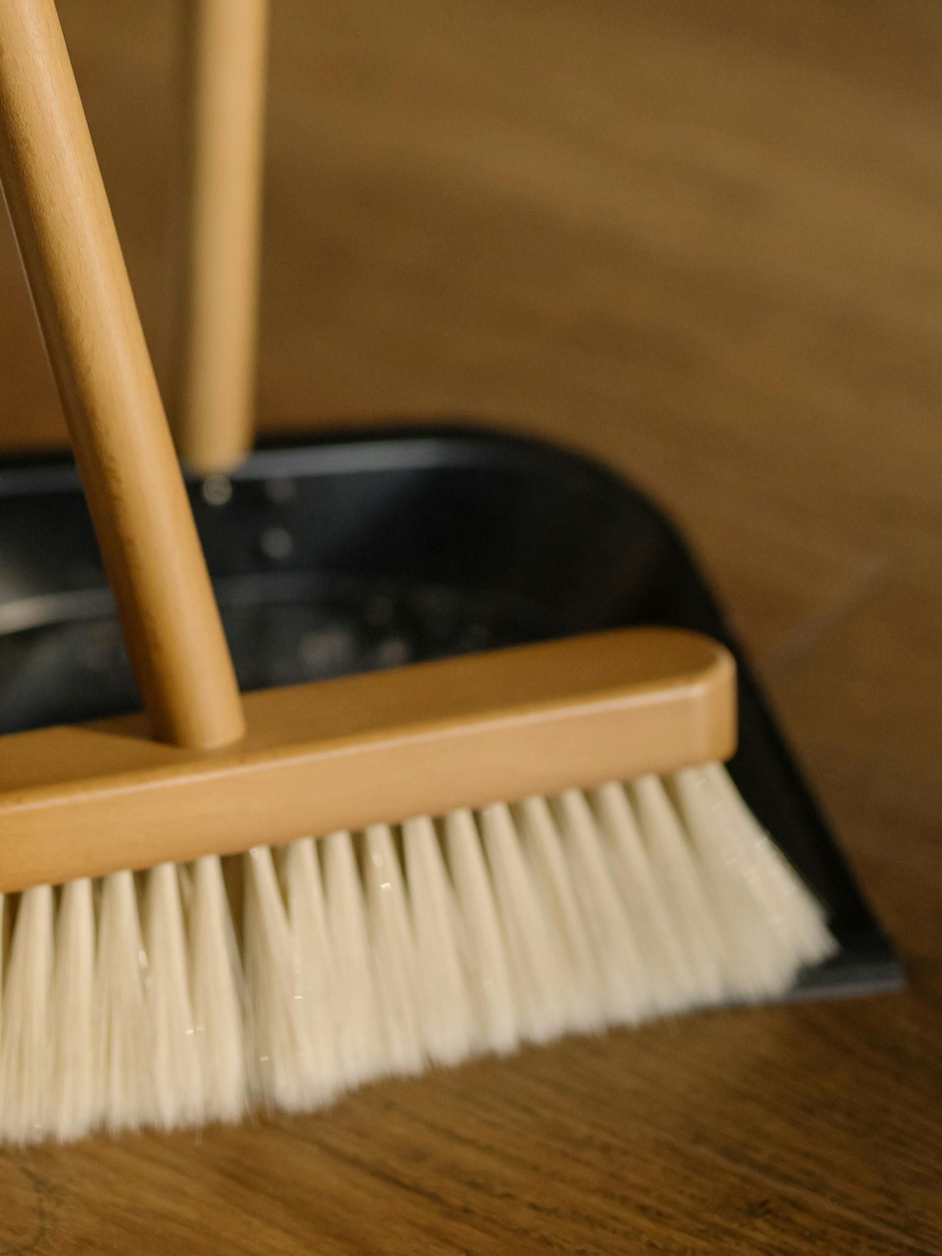 A close up of a broom and shovel on a wooden floor.