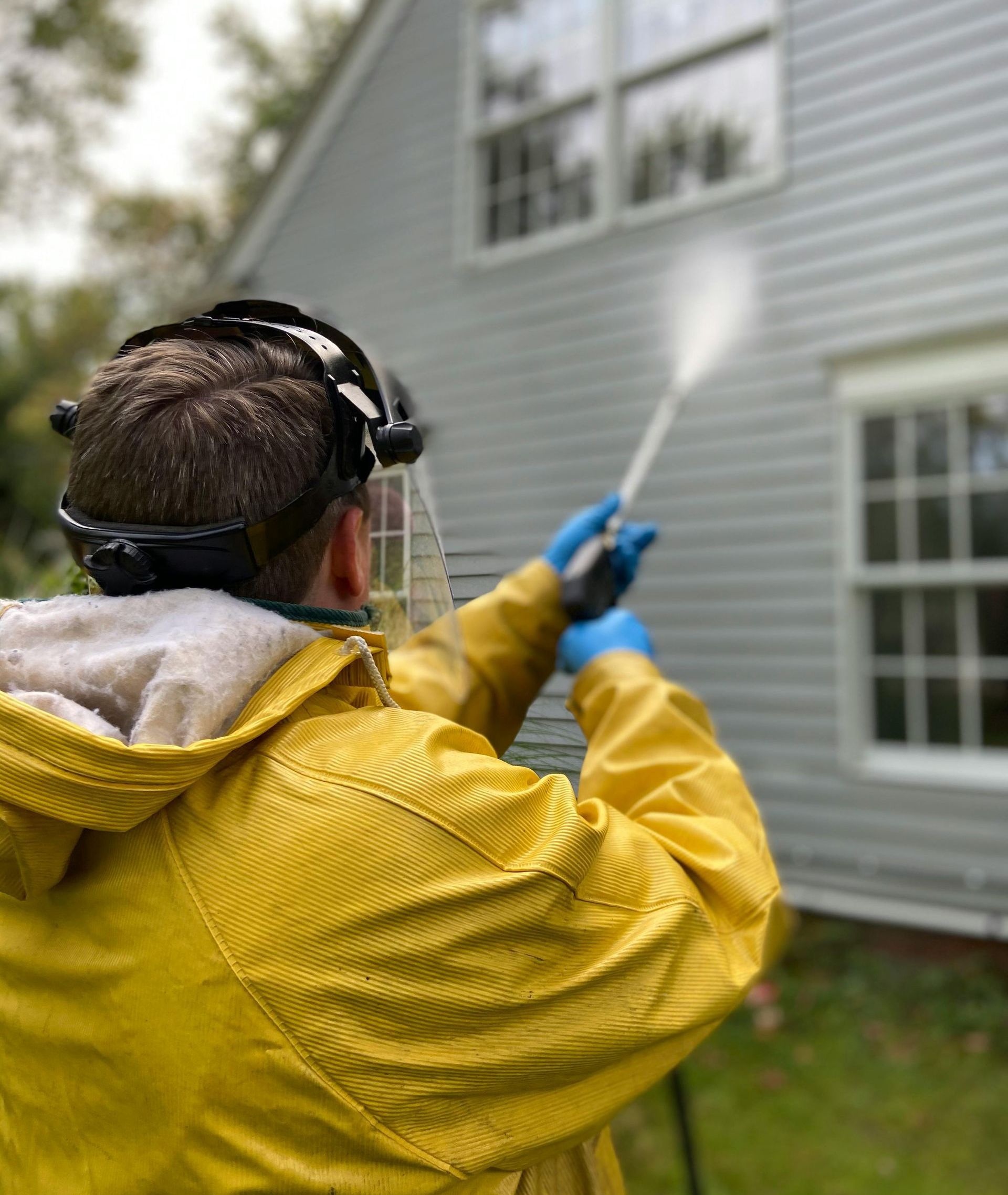 A man in a yellow jacket is power washing the side of a house.