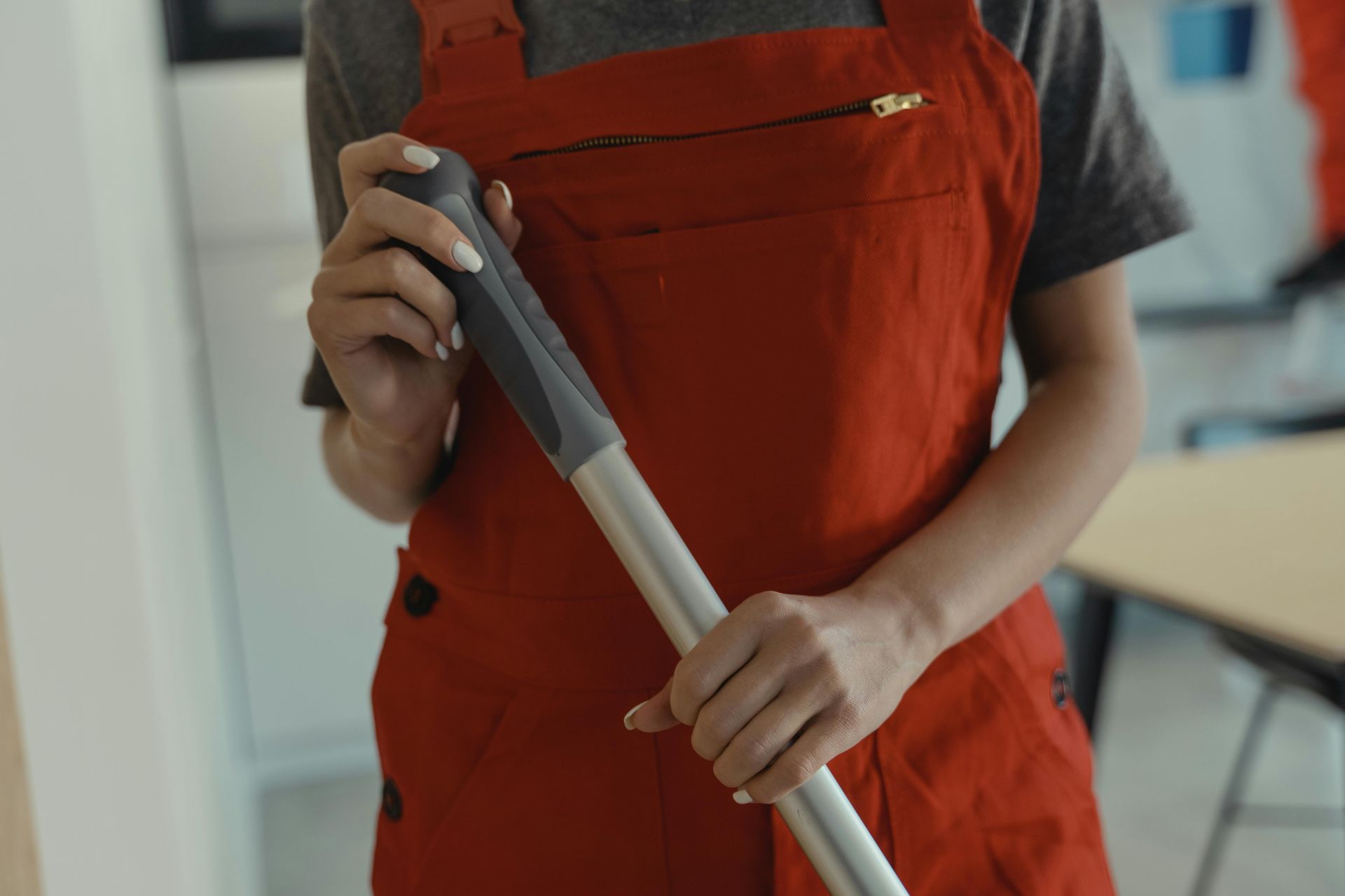 Person in red overalls holding a mop handle indoors