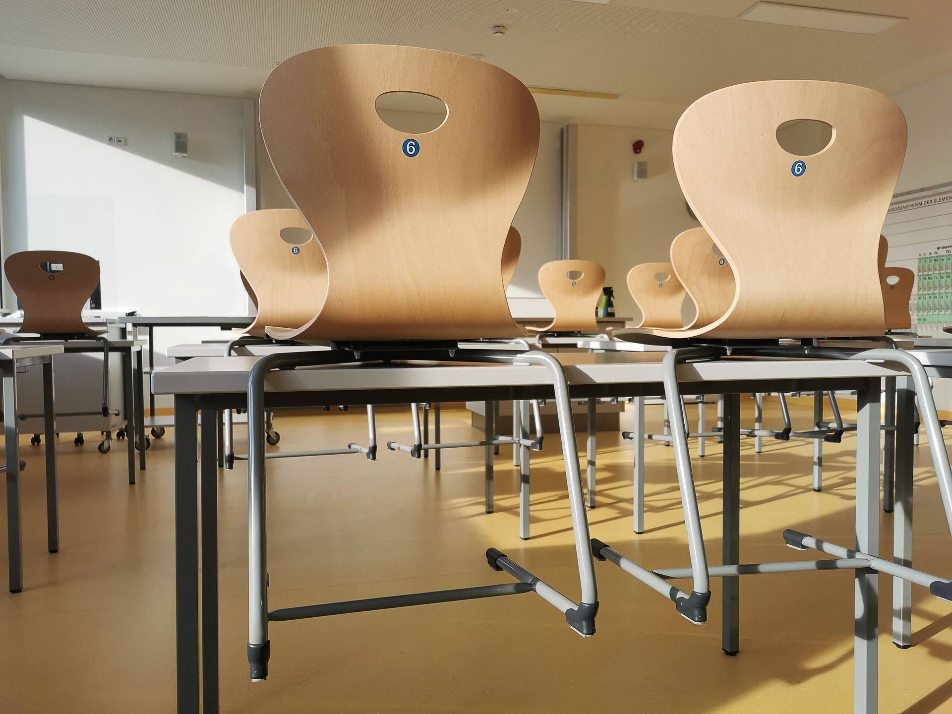 Empty classroom with wooden chairs on desks, viewed from a low angle.