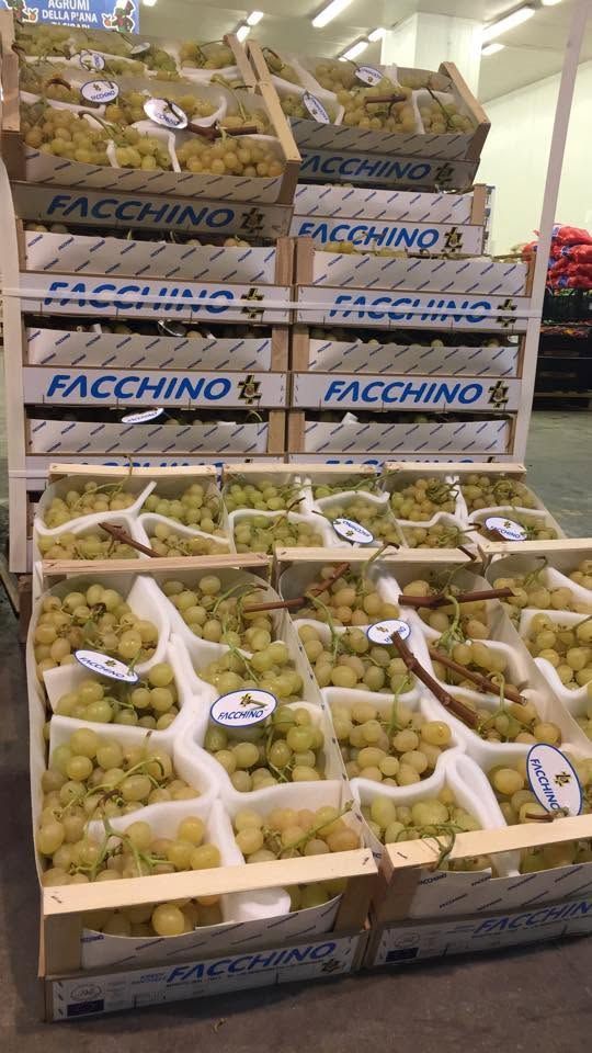 Pallet di uva verde in scatole e sacchi, impilati in una corsia di un magazzino o di un mercato ortofrutticolo