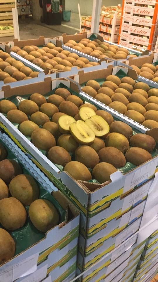 Cassette di kiwi al mercato, con uno tagliato a metà che ne mostra la polpa verde.