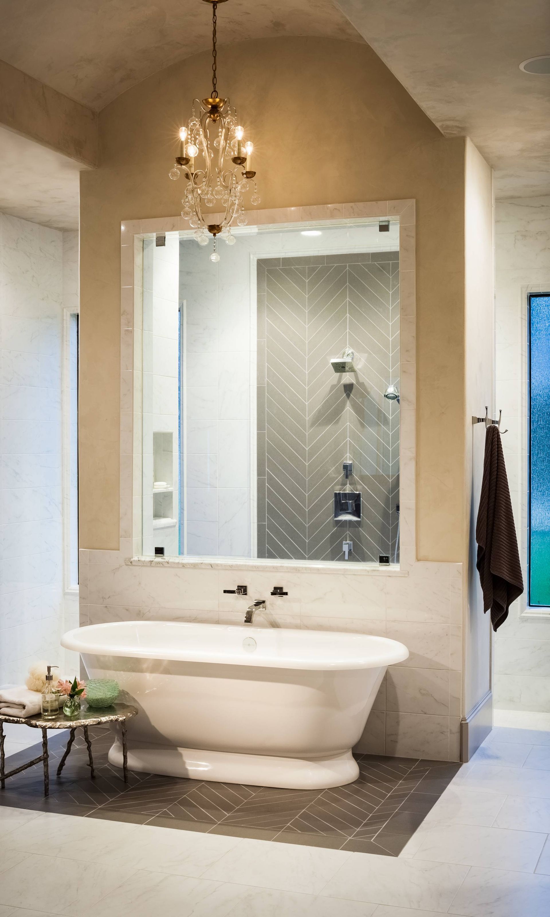 A bathroom with a bathtub , shower , mirror and chandelier.