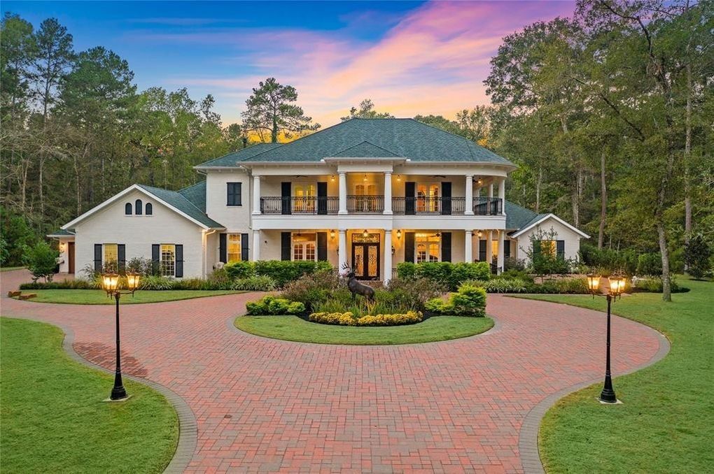 A large white house with a brick driveway and trees in the background.