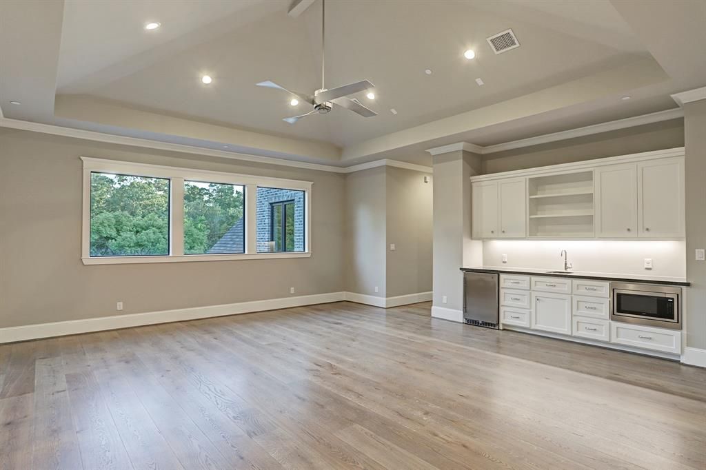 A large empty room with hardwood floors , white cabinets and a ceiling fan.