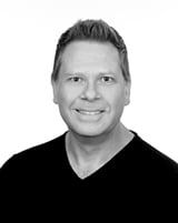 A man in a black shirt is smiling in a black and white photo.