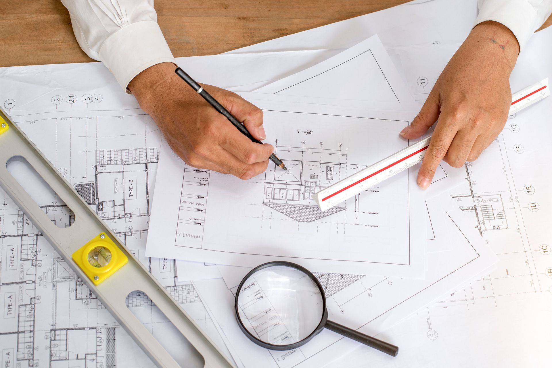 A person is working on a blueprint with a magnifying glass and a ruler.