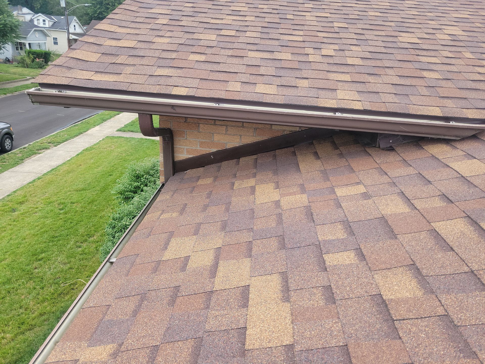 A high-angle view of a brown shingled roof with a gutter system and a junction where two roof sections meet.