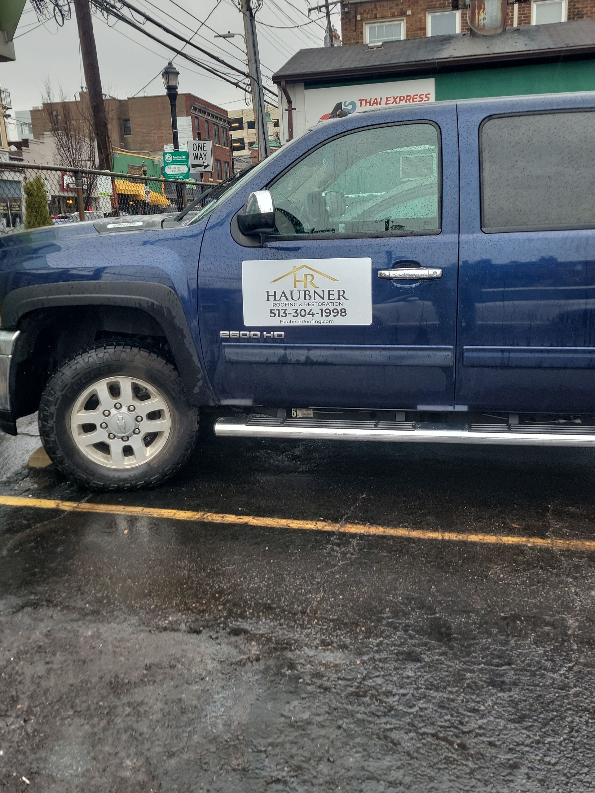 A blue pickup truck parked on an asphalt lot, featuring a white logo on the driver's side door.