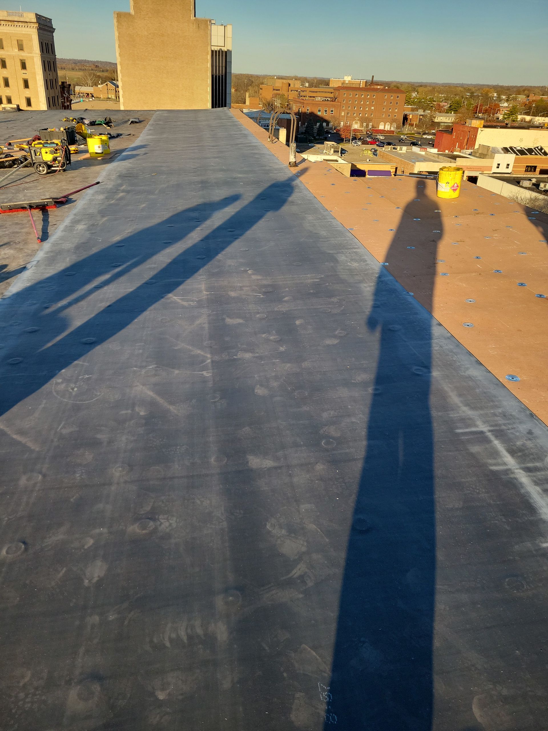 A rooftop view looking down a long, dark membrane surface with long shadows cast across the roof.