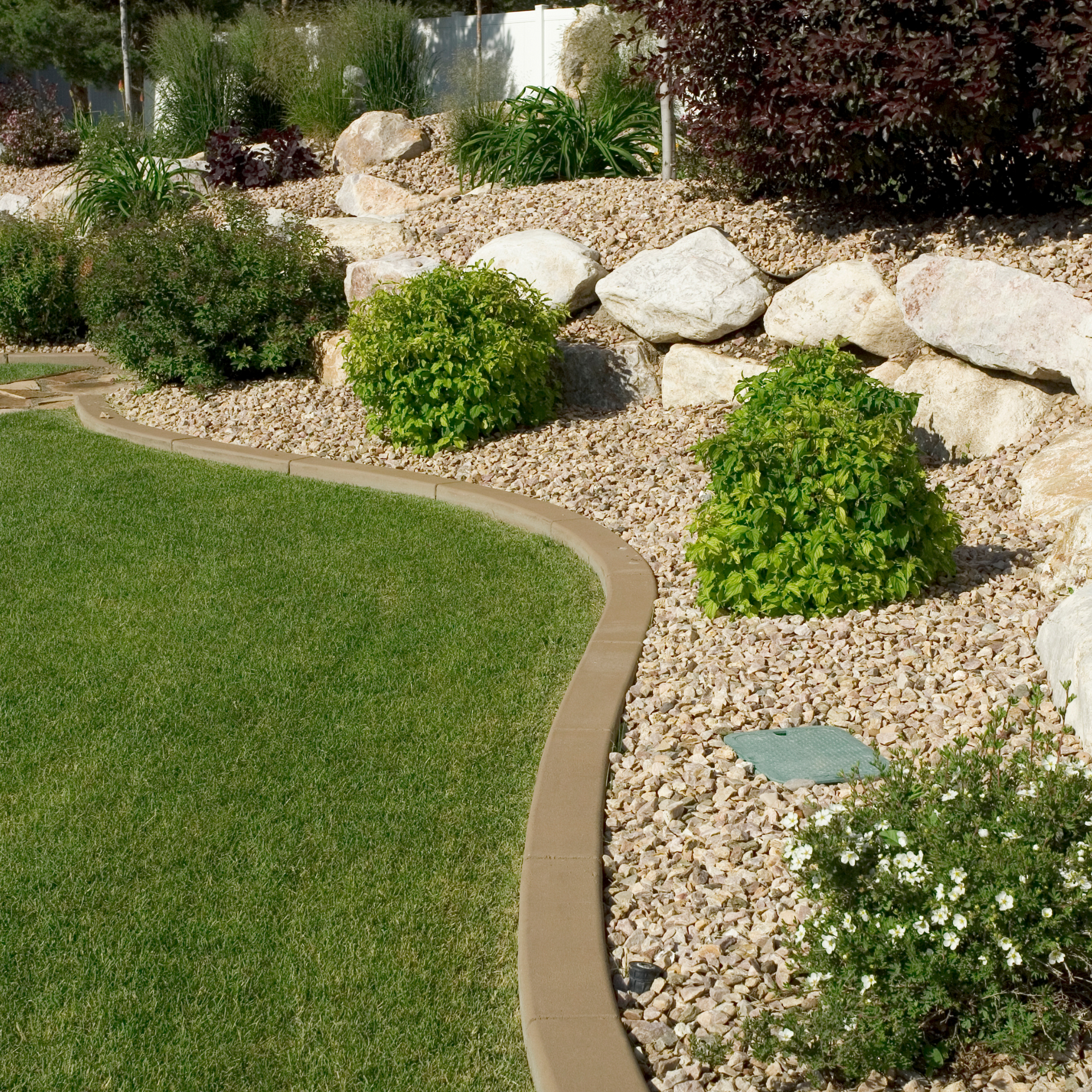 A lawn with a concrete curb surrounded by rocks and bushes