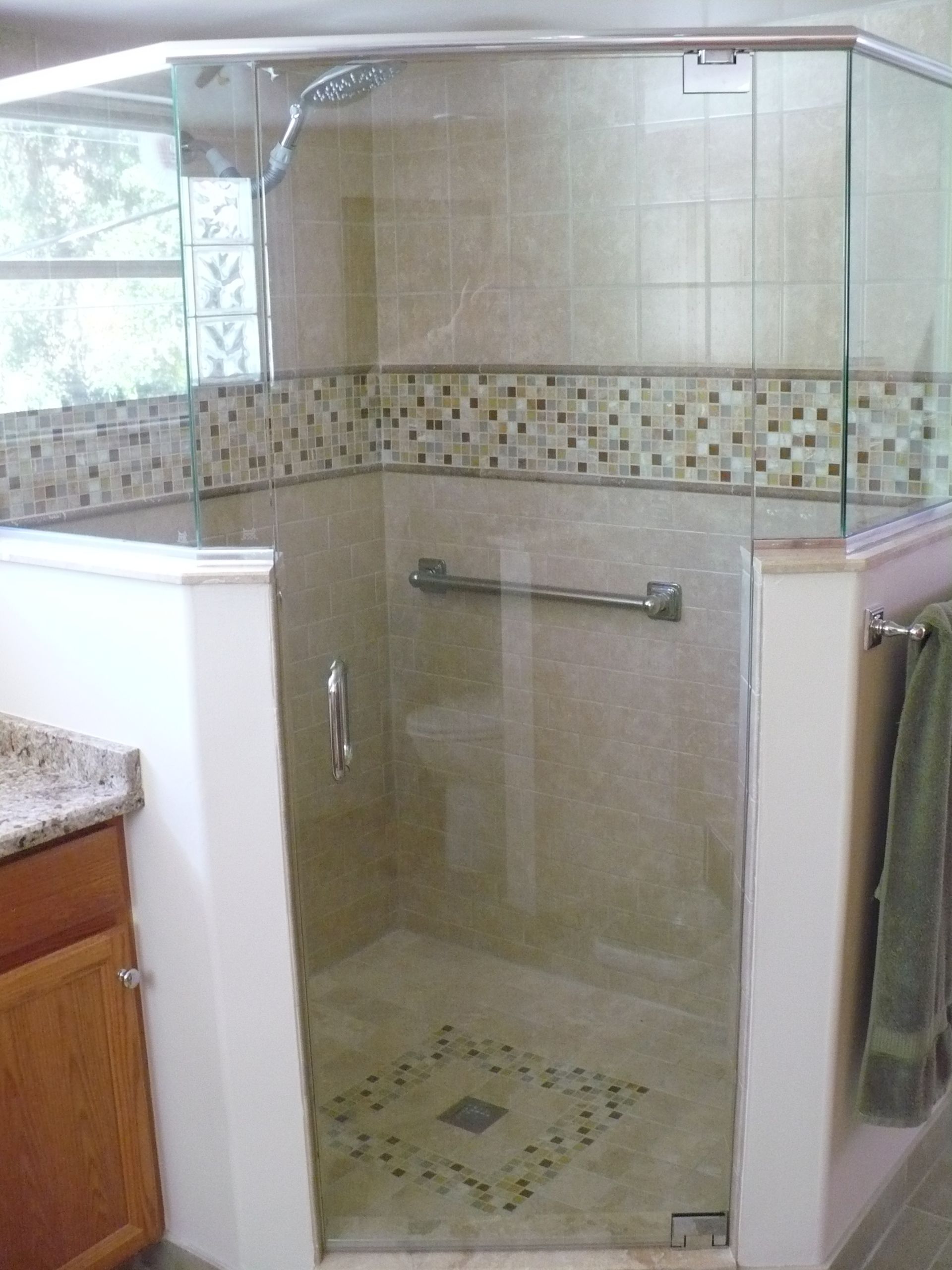 Glass shower stall in a tiled bathroom with a mosaic border and a grab bar.