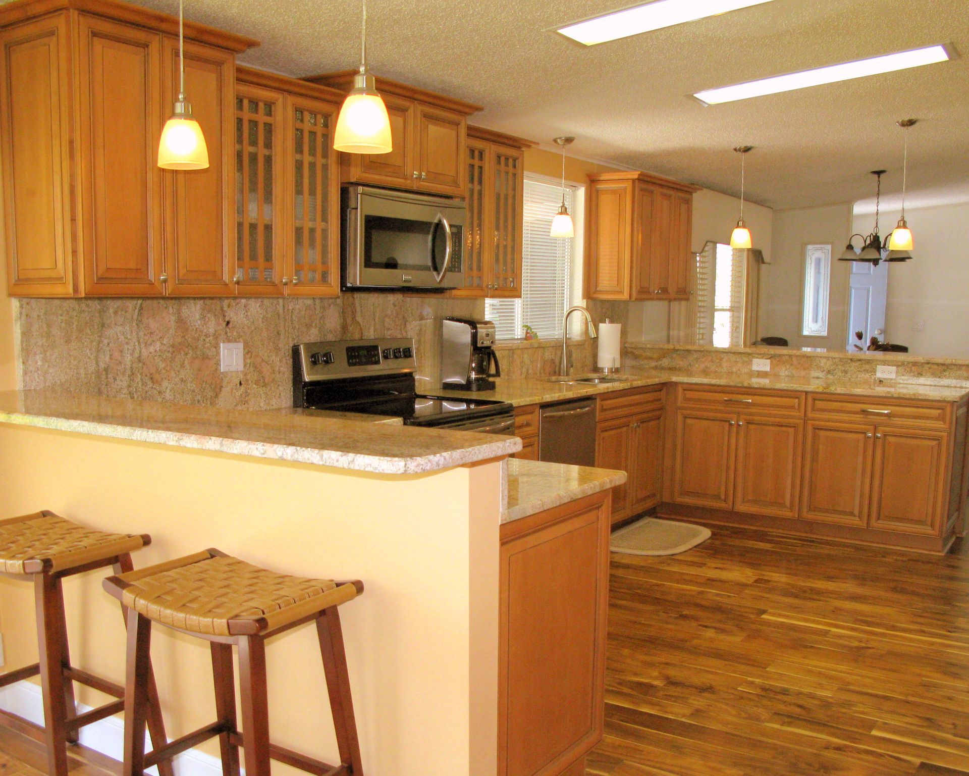 Modern kitchen with wooden cabinets, granite counters, hanging lights, and a breakfast bar with stools