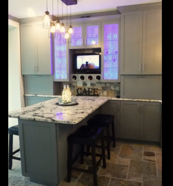 Modern kitchen with gray cabinets, marble island, pendant lights, and a TV above a “CAFE” backsplash