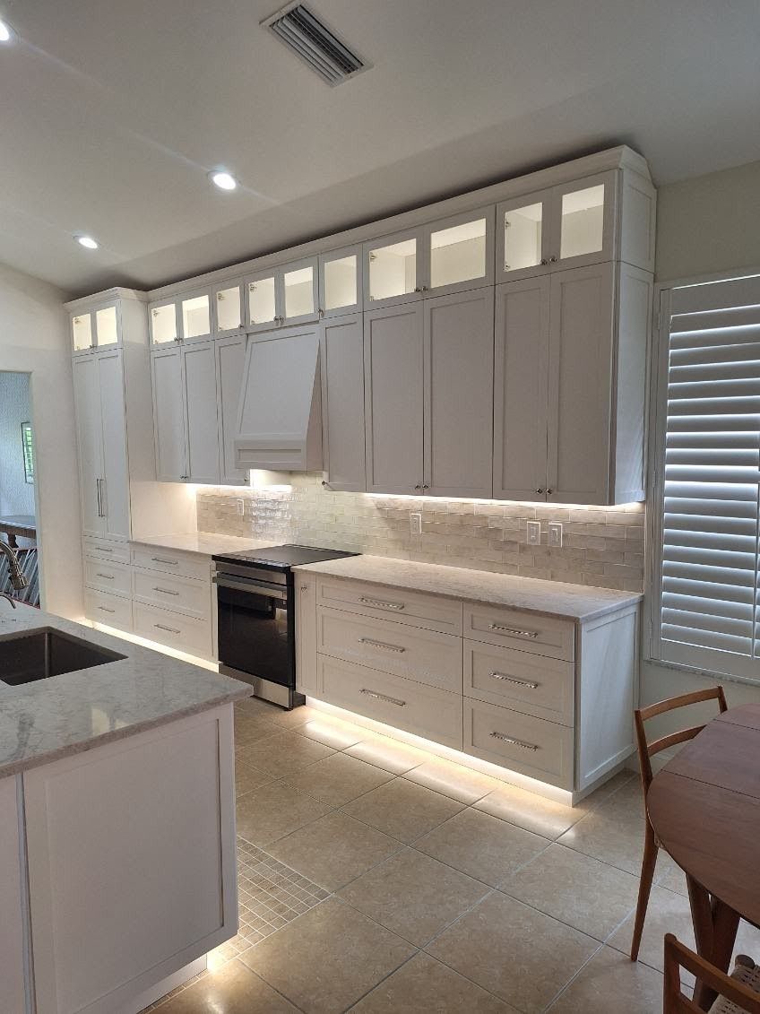 Bright modern kitchen with white cabinets, gray counters, tiled backsplash, and under-cabinet lighting.