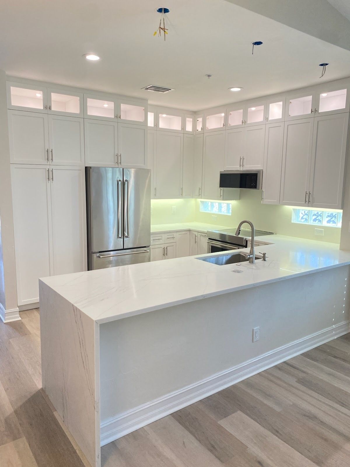 Bright modern kitchen with white cabinets, stainless fridge, large island, and recessed lighting