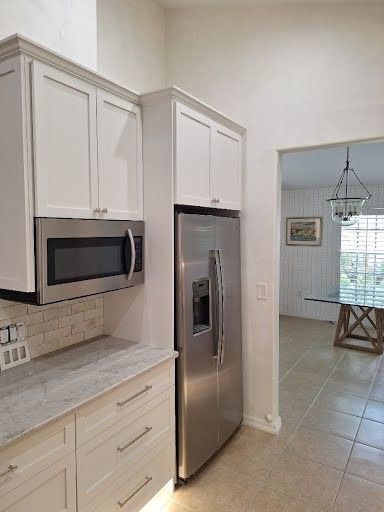 White kitchen with stainless steel appliances, granite countertop, and tile floor opening to a dining area.
