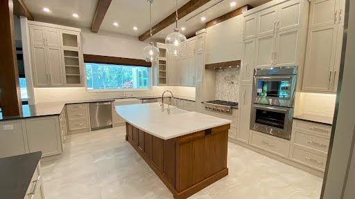 Bright modern kitchen with white cabinets, large island, built-in ovens, and wood ceiling beams