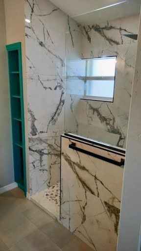 Marble-tiled bathroom with glass shower enclosure, small window, and black towel bars