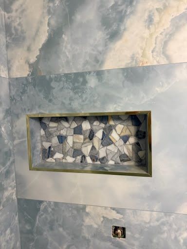 Small recessed wall niche with mosaic stone tiles set in a blue-gray textured wall.