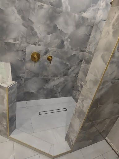 Marble-tiled shower with gold fixtures, white shower pan, and frameless glass door.