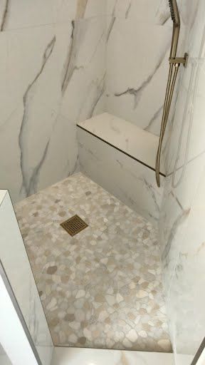 Small tiled shower stall with marble-look wall tiles, pebble floor, and built-in bench.