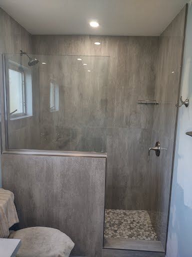 Walk-in shower with gray tile walls, glass door, and pebble floor in a modern bathroom