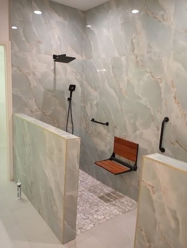 Accessible shower with wall-mounted seat, grab bars, and handheld showerhead in a tiled bathroom.