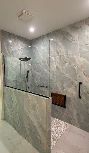 Modern tiled shower with glass partition, black fixtures, and built-in wood bench.