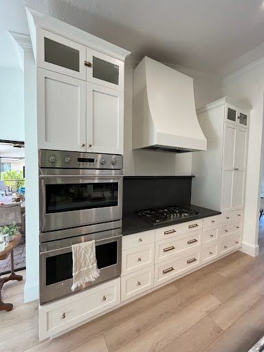 White modern kitchen with built-in double oven, gas cooktop, and tall cabinets.