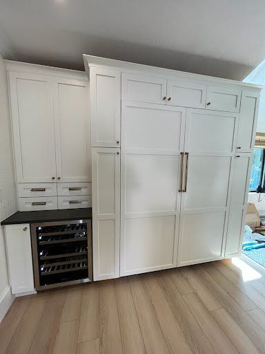 White built-in kitchen cabinets with a stainless wine cooler in a bright room with wood flooring