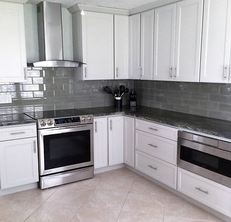 Modern white kitchen with stainless steel stove, range hood, dishwasher, and gray tile backsplash