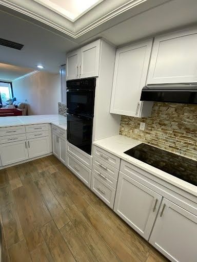 Bright white modern kitchen with wood floors, black built-in oven, and white cabinets.