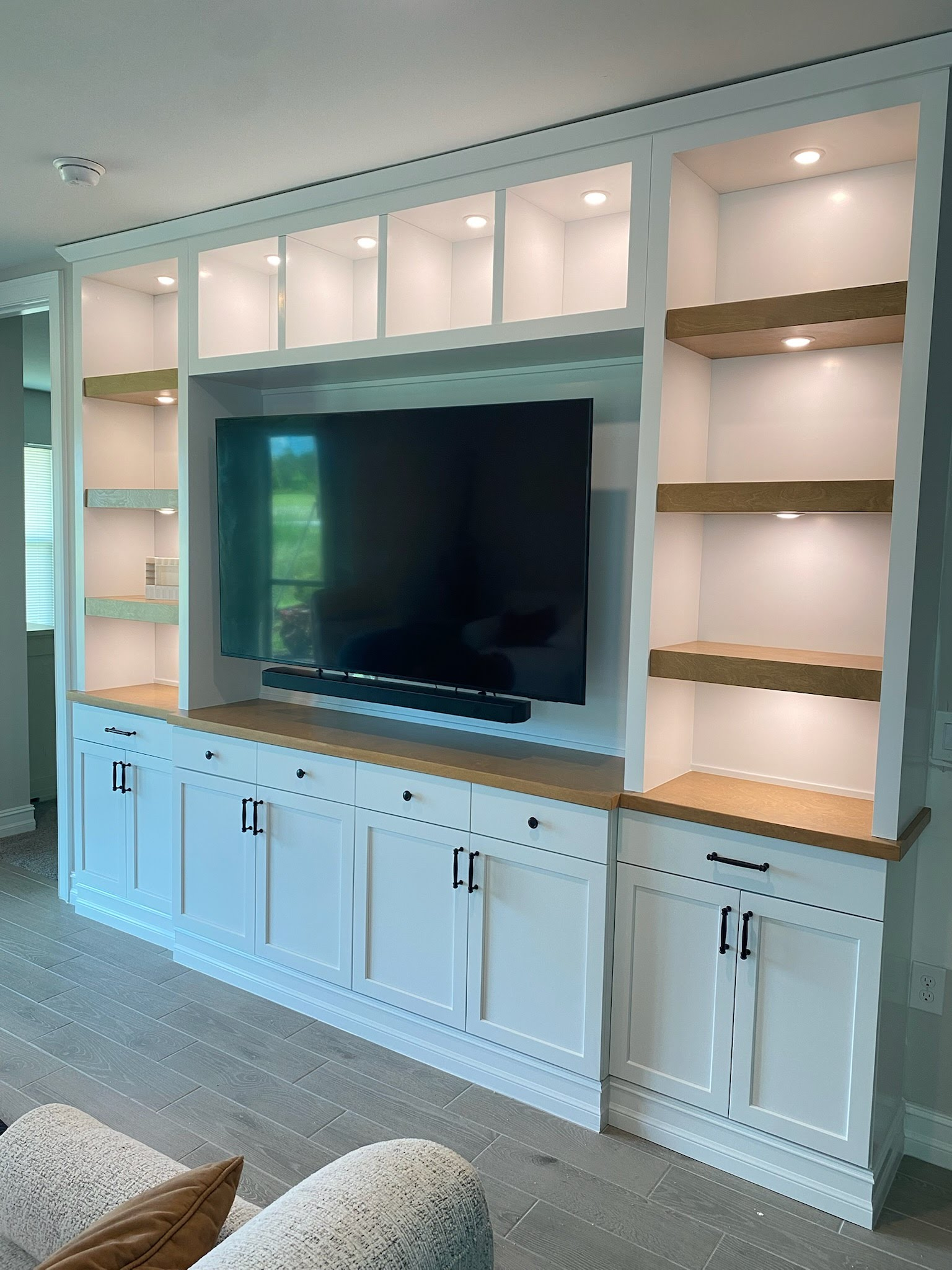 Built-in white entertainment wall with TV, shelves, and cabinets in a bright living room