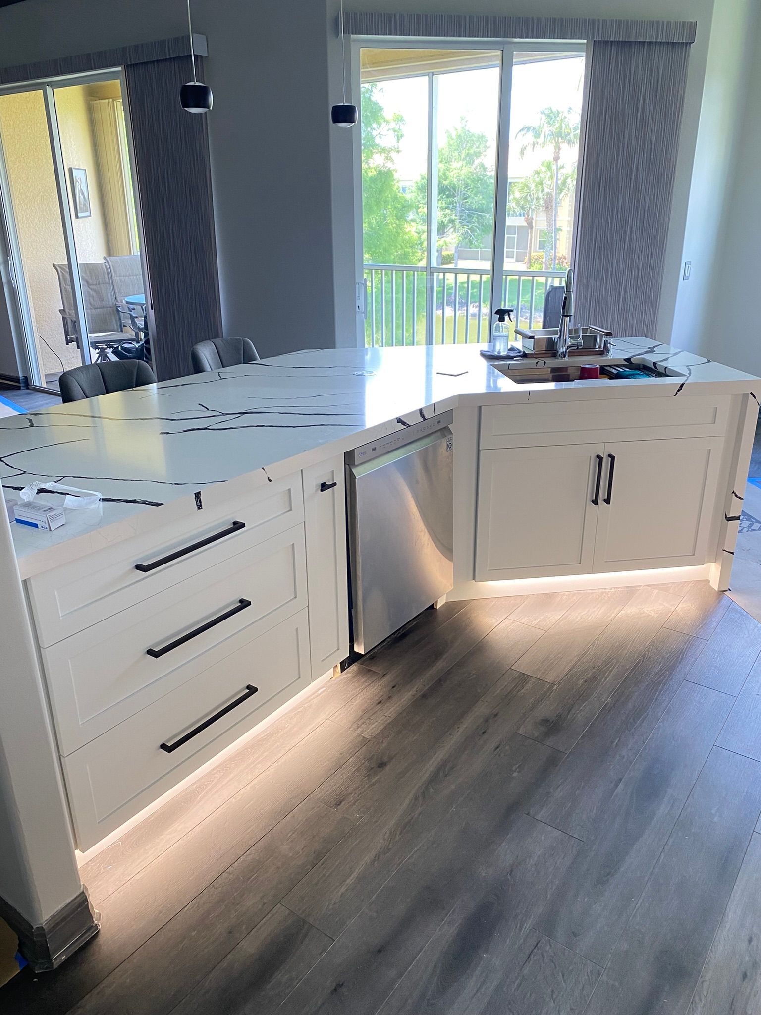 Bright white kitchen with L-shaped cabinets, peninsula, wood floor, and sliding glass doors to a balcony.