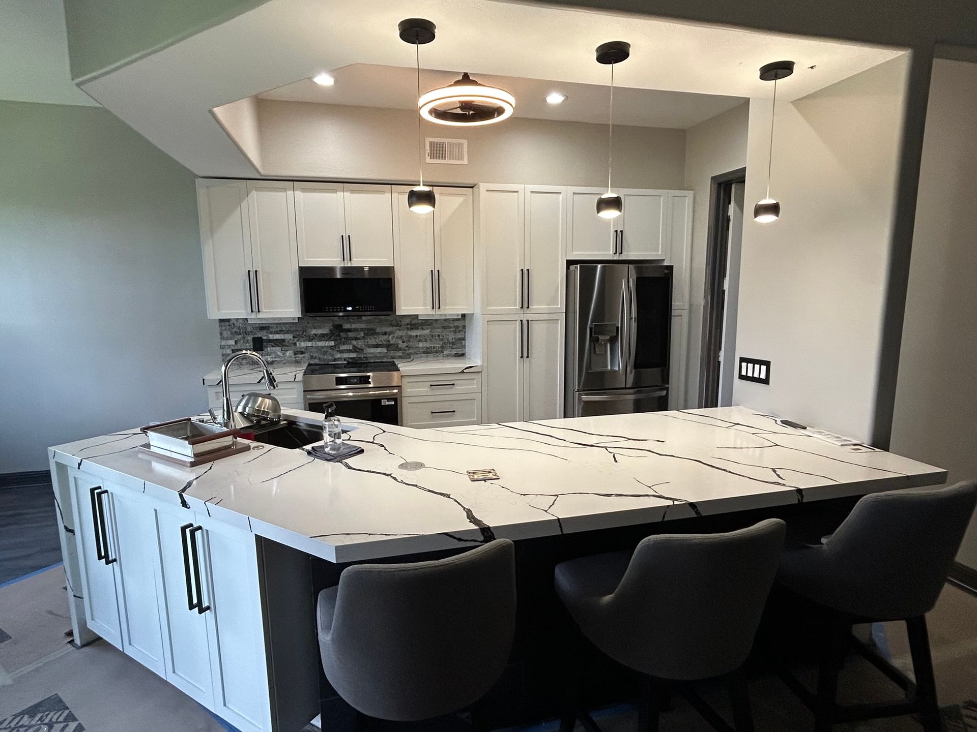 Modern kitchen with white cabinets, gray island, stainless fridge, and black barstools under pendant lights