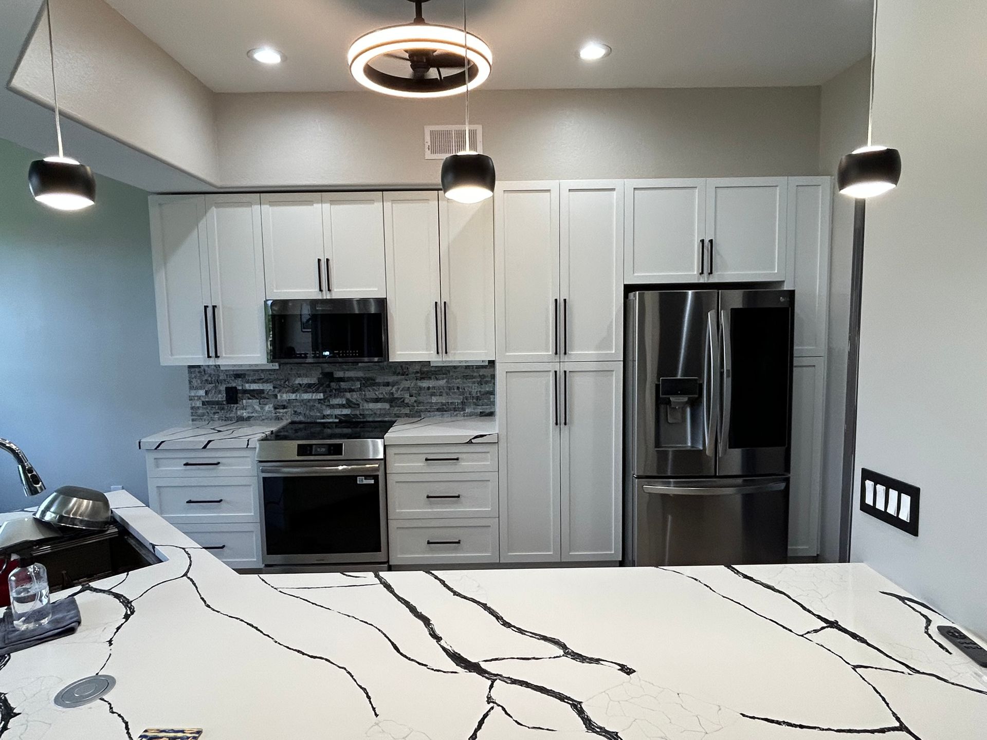 Modern kitchen with white cabinets, stainless steel appliances, and a marble island under pendant lights