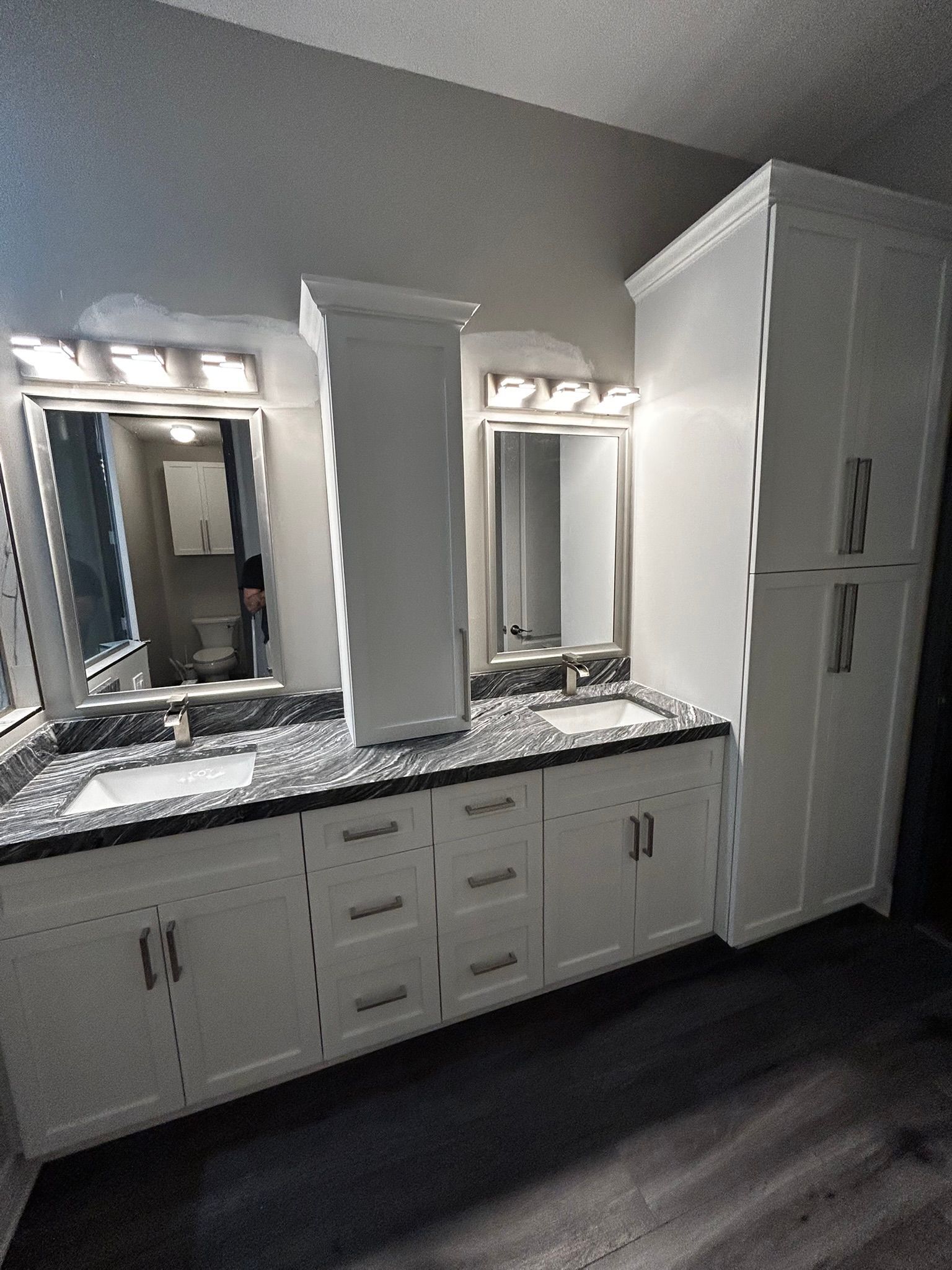 White bathroom vanity with double mirrors, granite countertop, and built-in cabinet against gray walls
