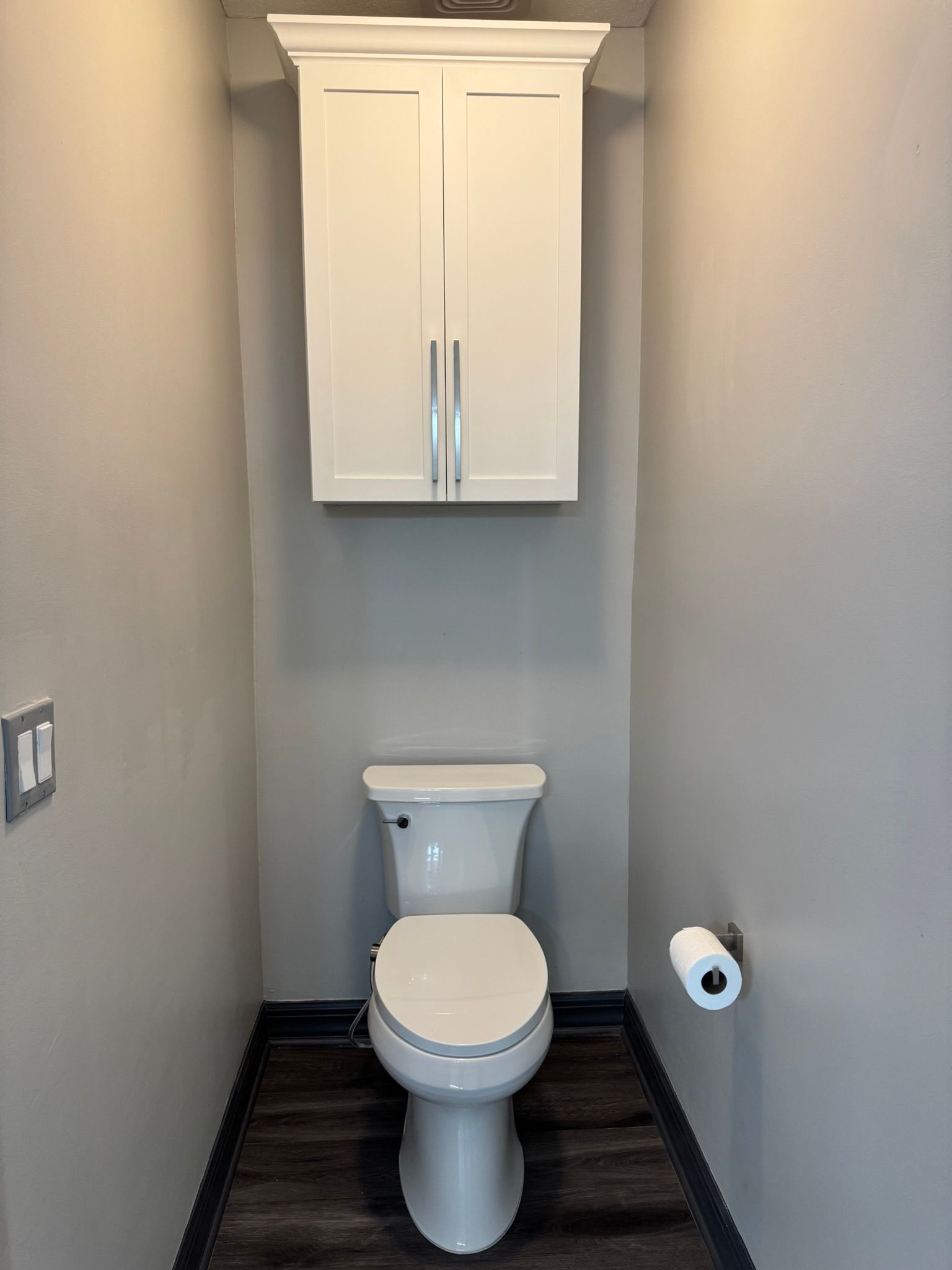 Small narrow bathroom with a white toilet, wall cabinet above, and toilet paper holder on the right.