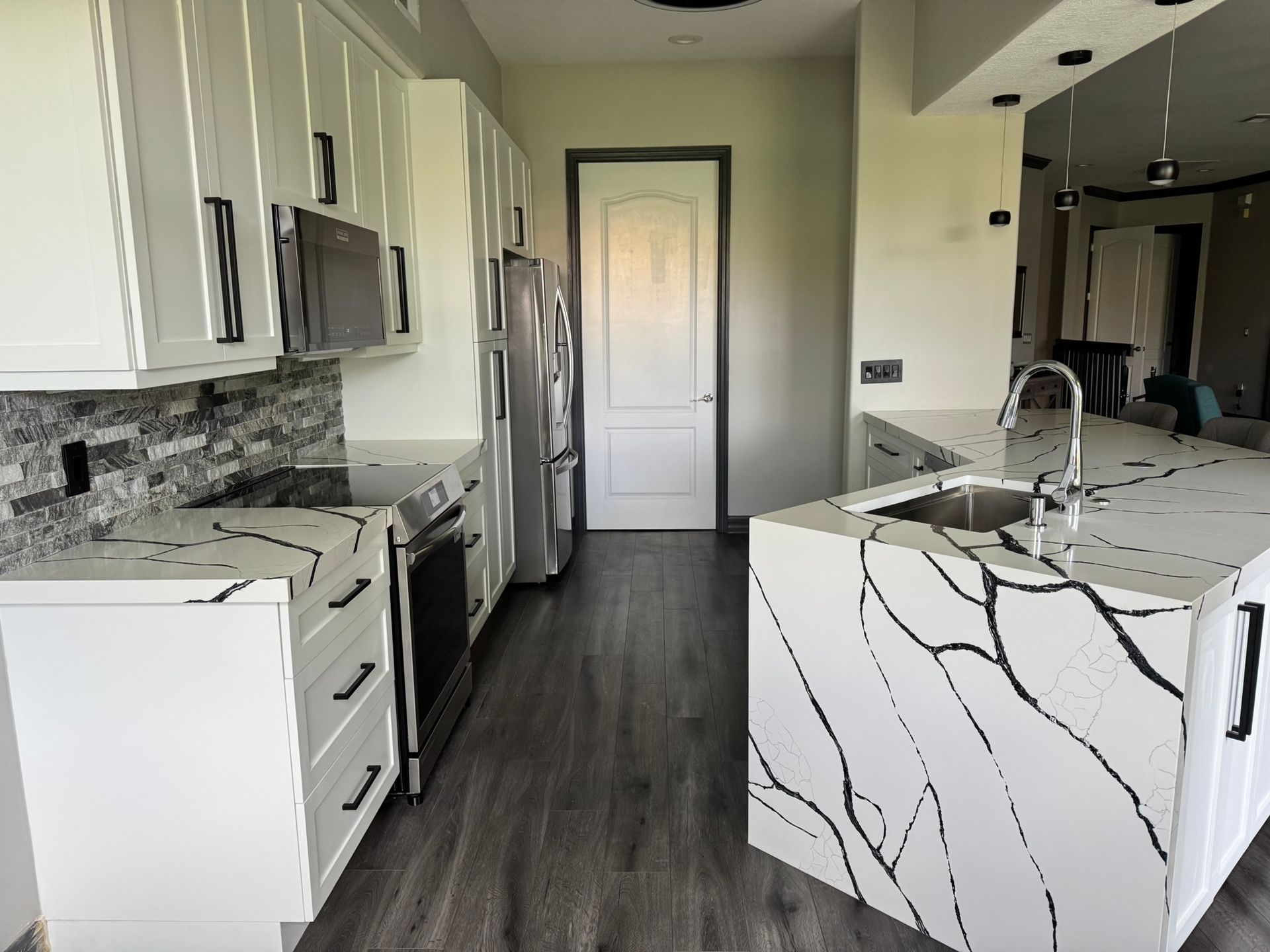 Modern kitchen with white cabinets, marble island, stainless appliances, and dark wood floor.