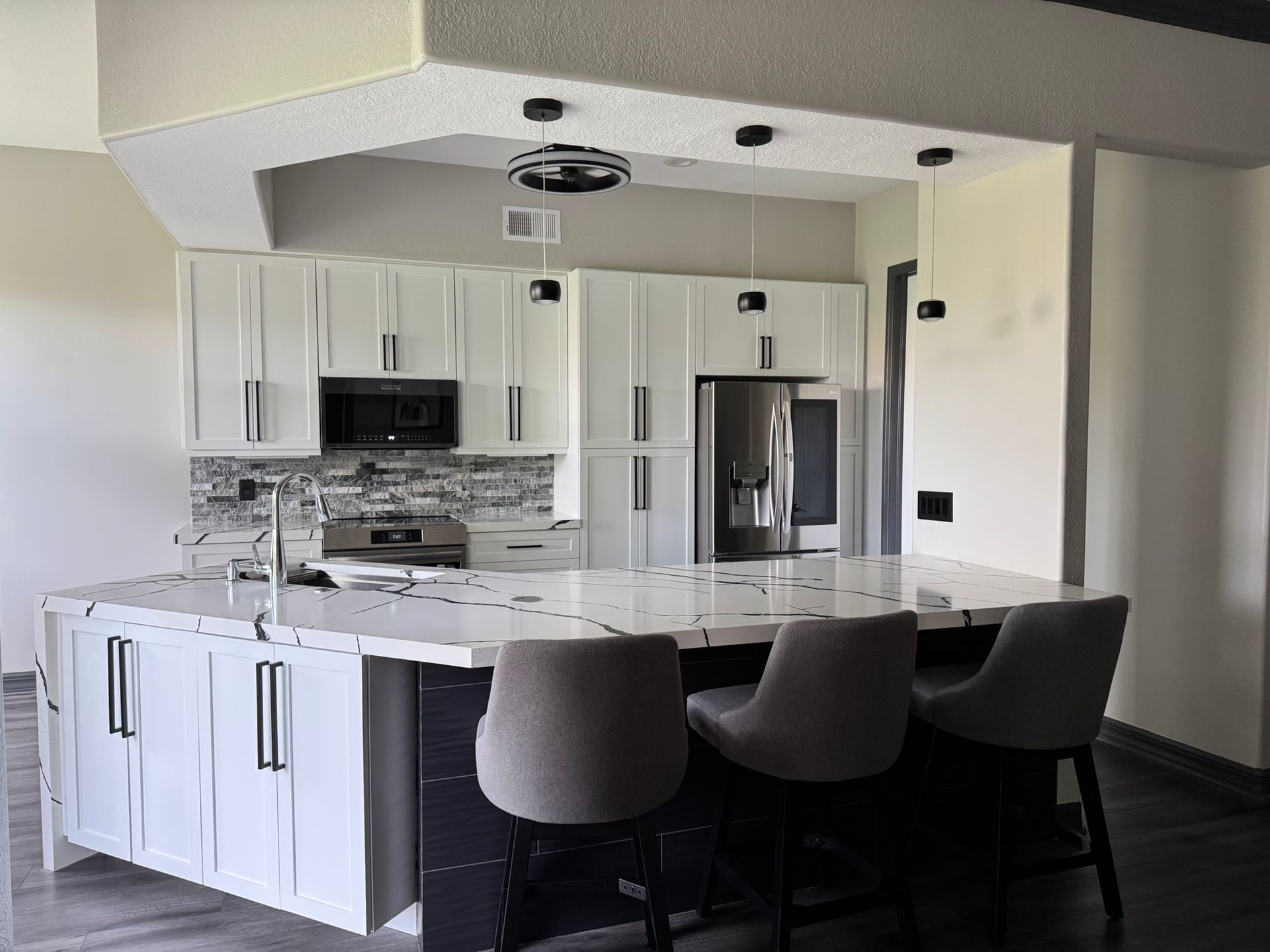 Modern kitchen with white cabinets, stainless steel appliances, island, and three dark barstools