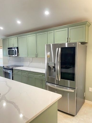 Modern kitchen with mint green cabinets, stainless steel appliances, and white marble island countertops