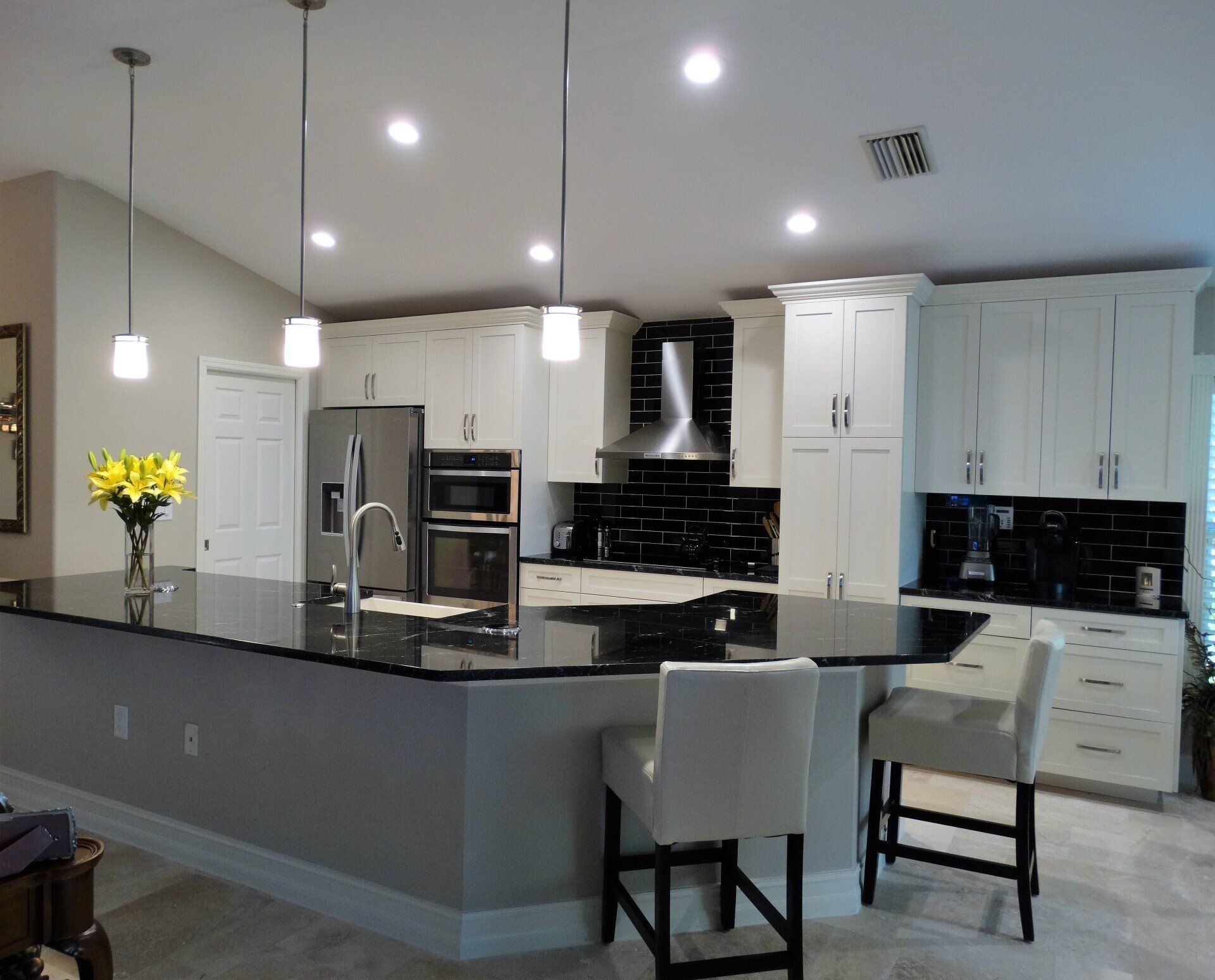 Modern open kitchen with gray island, pendant lights, white cabinets, and stainless steel appliances
