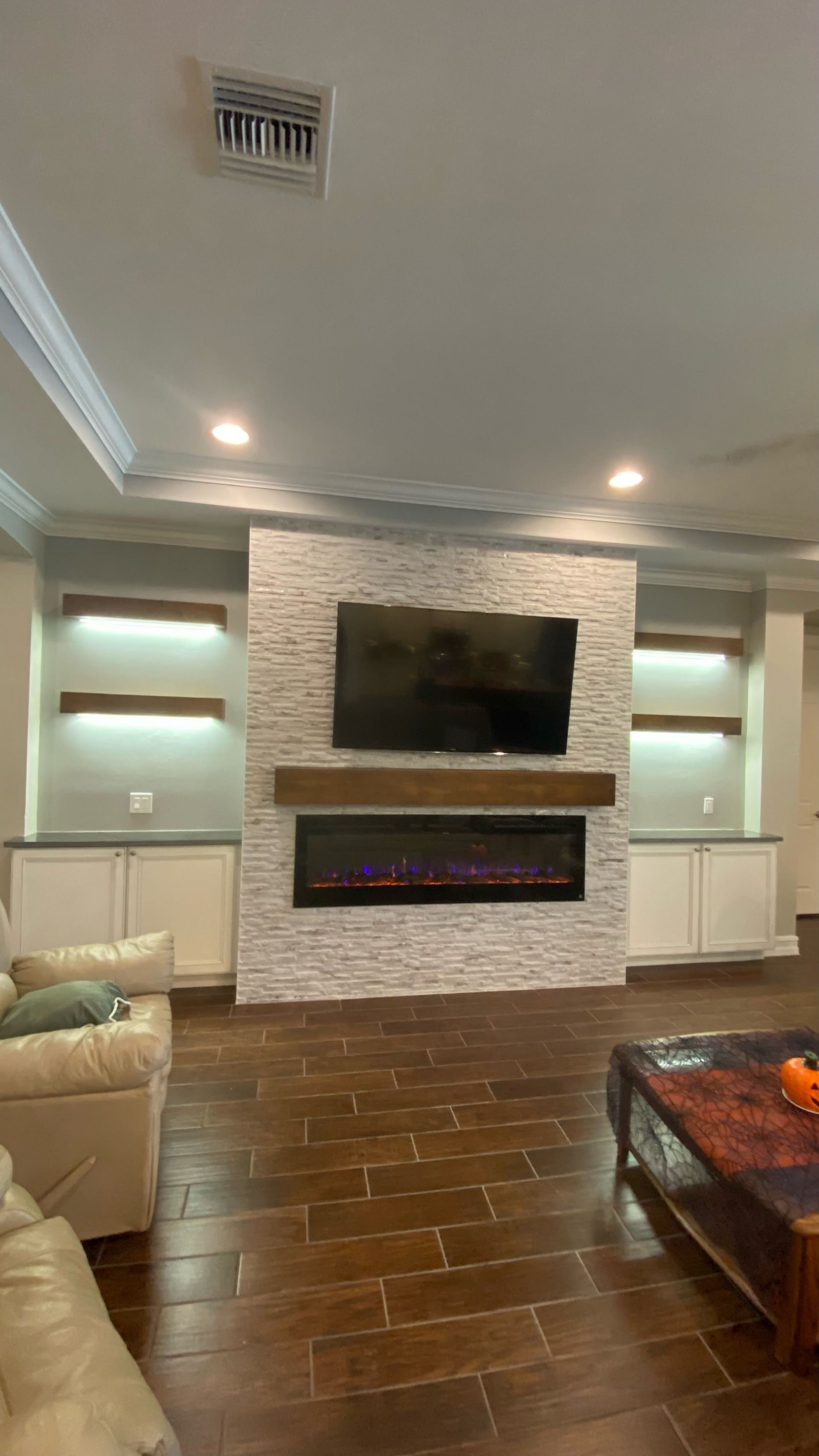 Modern living room with stone fireplace, mounted TV, recessed lights, and dark hardwood floors