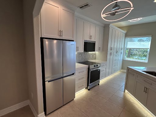 Bright modern kitchen with stainless steel appliances, white cabinets, and a large window.