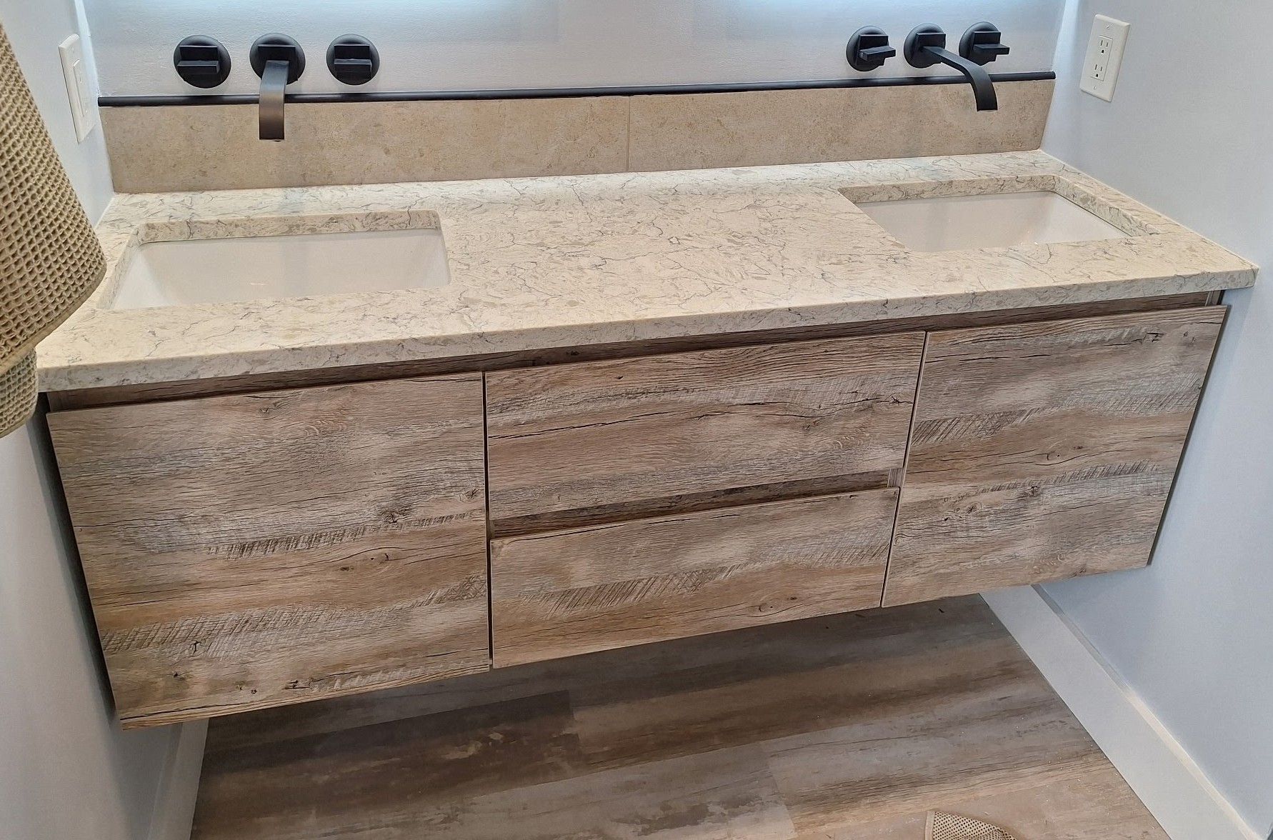 Modern bathroom vanity with double sinks and wood-look cabinets beneath a stone countertop.