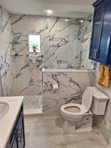 Modern bathroom with marble-look shower walls, blue cabinets, toilet, and walk-in shower.
