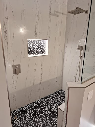 Modern shower with marble-look tile, pebble-pattern floor, and glass enclosure door