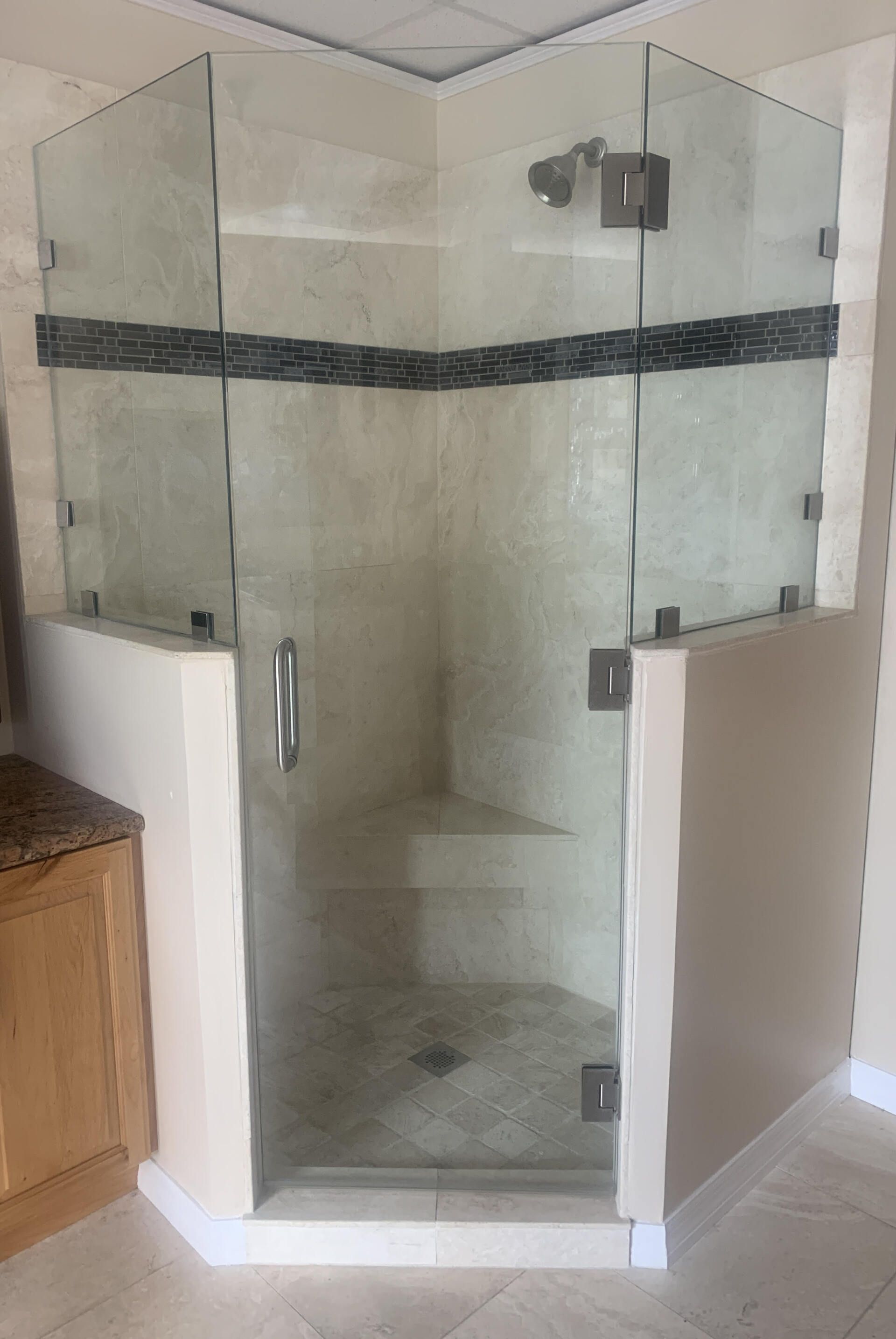 Glass corner shower enclosure with beige tile walls and dark accent band in a bathroom
