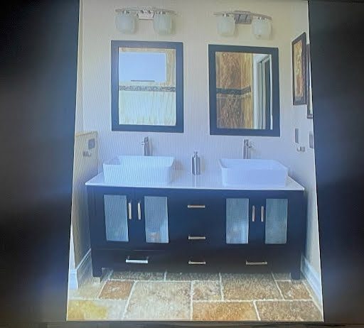 Modern bathroom with double sinks, black vanity, framed mirrors, and stone tile floor.